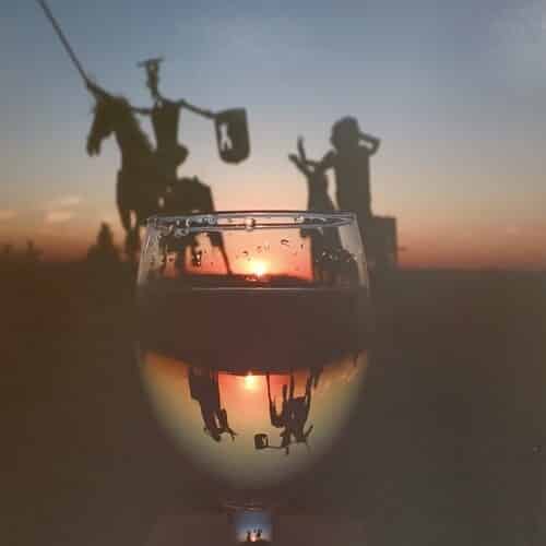 Don Quijote y Sancho inmortalizados en una estatua metálica vistos en un atardecer al trasluz de una copa de agua