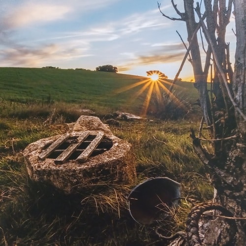 brocal de piedra de pozo y cubo de chapa+horizonte+puesta de sol+ladera de trigo verde