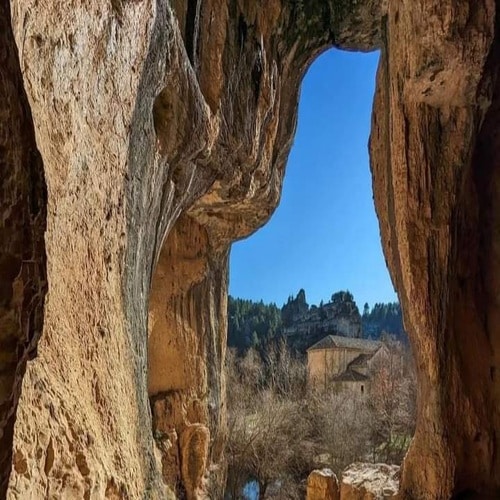 Entrada a una caverna de piedra con caserío y río al fondo