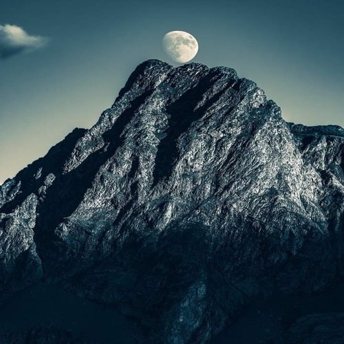 Cumbre de una montaña y luna llena en su cumbre en lo alto del cielo