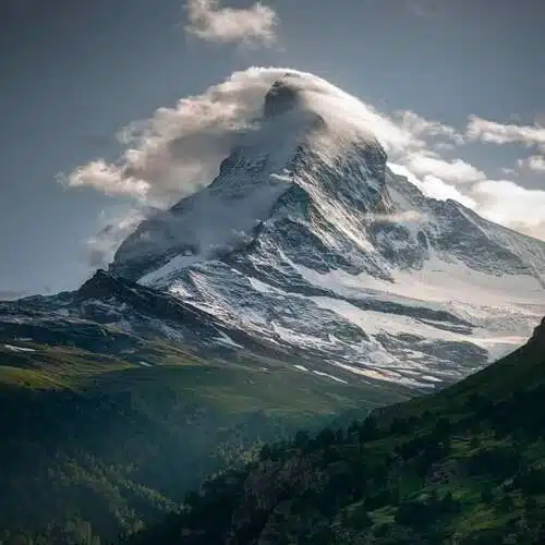 Montaña cubierta de nubes, rodeada de un valle de pinos